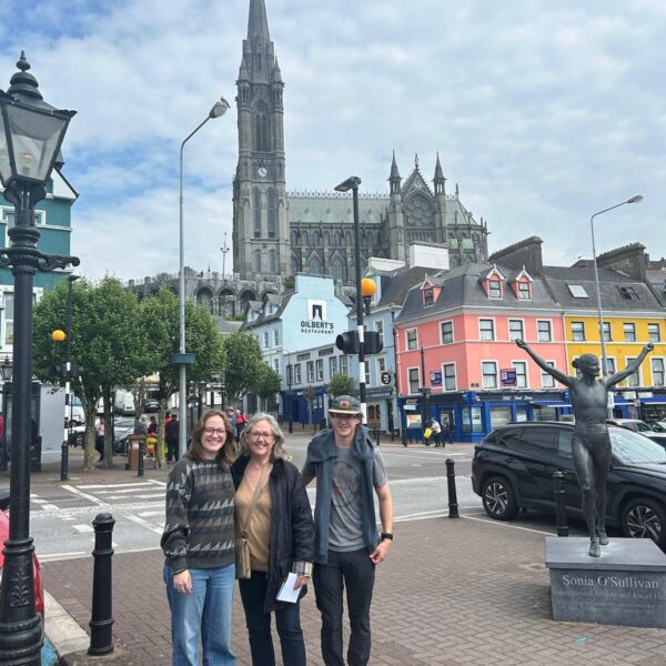Three people posing in the centre of Cobh, with streets and the cathedral in the background.