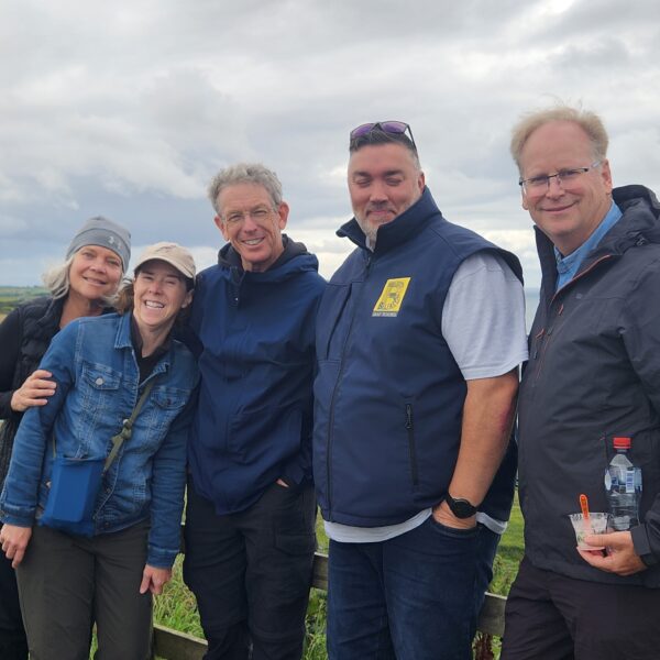 Group of 5 people by a fence overlooking the sea, with landscape visible.
